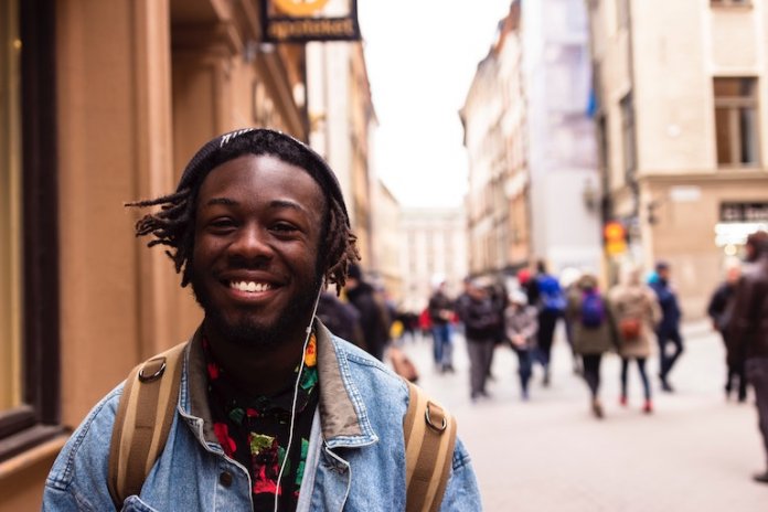 Lächelnder Student, der auf einer Straße geht, während er Musik hört